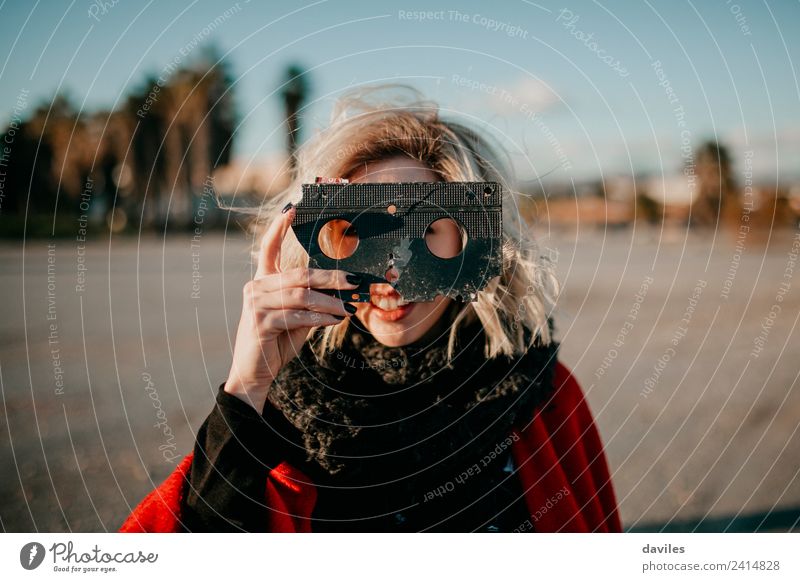 Lächelndes blondes Mädchen, das ein altes kaputtes Videoband in der Hand hält und bei Sonnenuntergang durch die Löcher schaut. Lifestyle Freude Glück schön