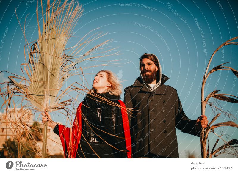 Blonde Frau und bärtiger Mann posieren bei Sonnenuntergang mit Pflanzenzweigen in der Hand und blauem Himmel im Hintergrund. Lifestyle Freude Freizeit & Hobby