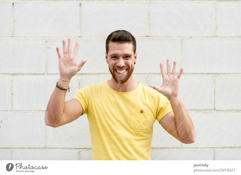 Lustiger junger Mann an der Ziegelwand mit offenen Händen Lifestyle Stil Glück Mensch Junger Mann Jugendliche Erwachsene Hand 1 18-30 Jahre Straße Mode T-Shirt