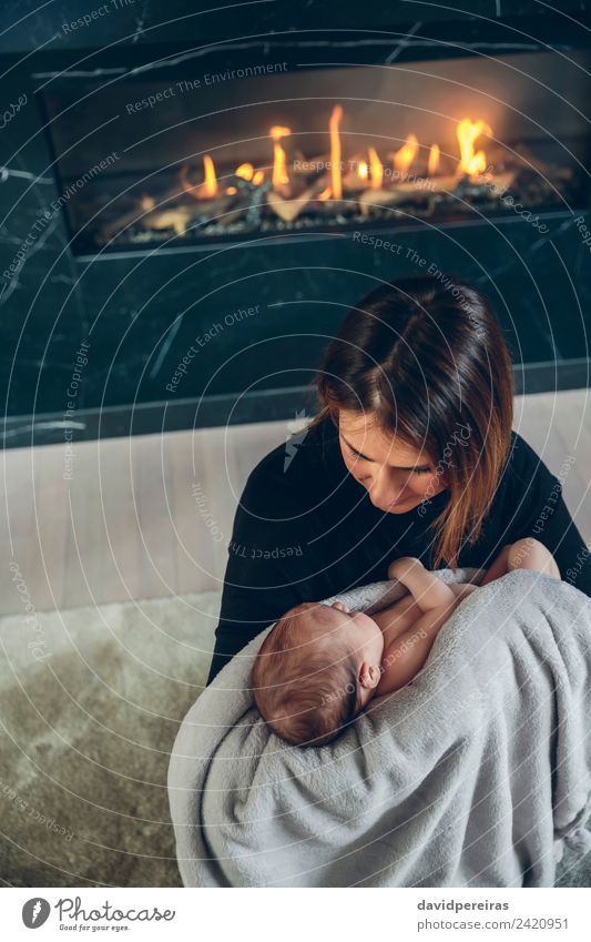 Mutter umarmt ihr Baby vor dem Kamin. Lifestyle schön Wohnzimmer Kind Mensch Frau Erwachsene Familie & Verwandtschaft Wärme Fluggerät Liebe schlafen Umarmen