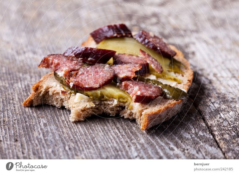 bites me Lebensmittel Wurstwaren Brot Ernährung Frühstück Holz ruhig Wurstbrot Brotscheibe Salami Gurkenscheibe Holzbrett Gewürzgurke beißen Snack landjaeger