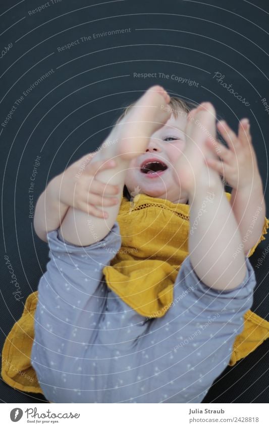 Kleinkind Trampolin lachen Füße Hände liegen feminin Kindheit 1 Mensch 1-3 Jahre Hose Kleid Fröhlichkeit lustig gelb grau schwarz Freude Lebensfreude Farbfoto