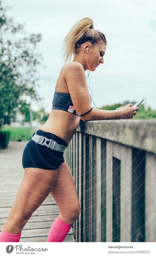 Frau in Sportbekleidung mit Kopfhörern, die wie ein Smartphone aussehen. Lifestyle Musik Joggen Telefon PDA Technik & Technologie Mensch Erwachsene Hand Park