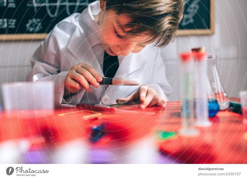 Glückliches Kind, das durch die Lupe flüssig aussieht. Flasche Freude Spielen Wohnung Tisch Wissenschaften Schule Klassenraum Tafel Labor Mensch Junge Lächeln