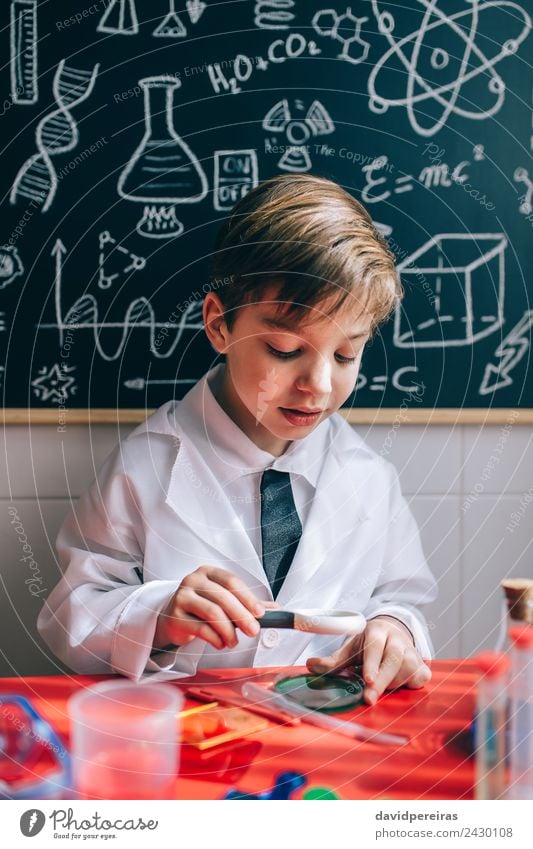 Glückliches Kind, das durch die Lupe flüssig aussieht. Flasche Freude Spielen Wohnung Tisch Wissenschaften Schule Klassenraum Tafel Labor Mensch Junge Kindheit