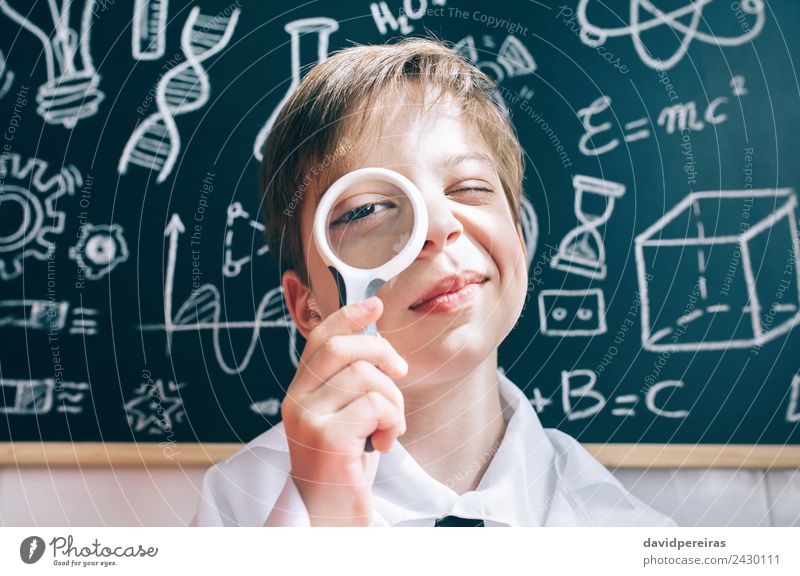 Kleiner Junge schaut durch die Lupe auf die Kamera. Freude Glück Spielen Wohnung Wissenschaften Kind Schule Klassenraum Tafel Labor Mensch Kindheit Lächeln