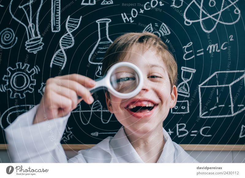 Glückliches Kind, das durch die Lupe auf die Kamera schaut. Freude Spielen Wohnung Wissenschaften Schule Klassenraum Tafel Labor Mensch Junge Kindheit Zähne