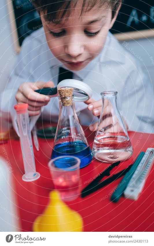 Glückliches Kind, das durch die Lupe flüssig aussieht. Flasche Freude Spielen Wohnung Tisch Wissenschaften Schule Klassenraum Tafel Labor Mensch Junge Kindheit