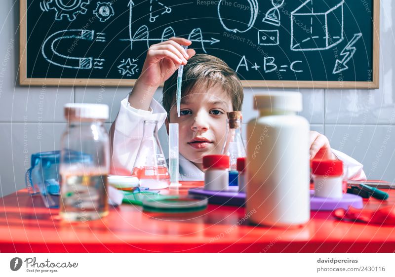 Kind spielt mit chemischen Flüssigkeiten über dem Tisch. Flasche Glück Spielen Wohnung Wissenschaften Klassenraum Tafel Labor Mensch Junge Kindheit Hand