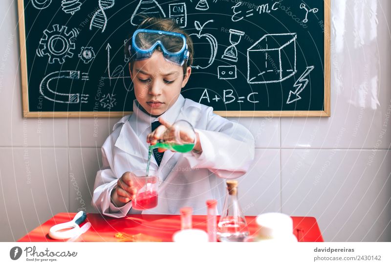 Ernsthaftes Kind beim Spielen mit chemischen Flüssigkeiten Flasche Glück Wohnung Tisch Wissenschaften Klassenraum Tafel Labor Mensch Junge Kindheit Hand