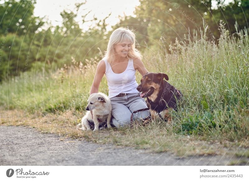 Blonde Frau mit ihren beiden Hunden auf dem Land Glück Gesicht Sommer Erwachsene Freundschaft 1 Mensch 45-60 Jahre Tier Wärme Gras Wiese blond Haustier Lächeln