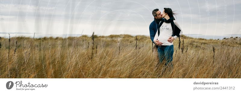 Schwanger mit Partner küssend und haltend Bauch Lifestyle Mensch Frau Erwachsene Mann Mutter Paar Landschaft Wind Gras Wiese Schal berühren Küssen Liebe Umarmen