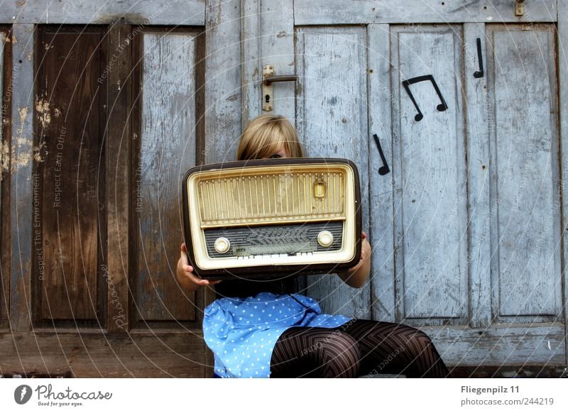 retro gestylte junge Frau posiert mit Radio vor altem Holztor. Musik Noten. Röhrenradio Stil Lautsprecher Radiogerät Junge Frau Jugendliche 1 Mensch Musik hören