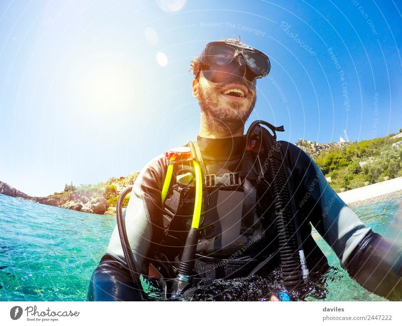 Glücklicher Mann, der Tauchkleidung und -ausrüstung trägt und lächelt, während er am Strand aus dem Wasser steigt. Lifestyle Freude Gesicht Erholung