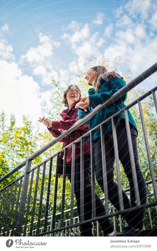 fröhliche Zwillingsschwestern stehen lachend auf einer Brücke und schauen nach oben Lifestyle Stil Freude Glück Mensch feminin Junge Frau Jugendliche