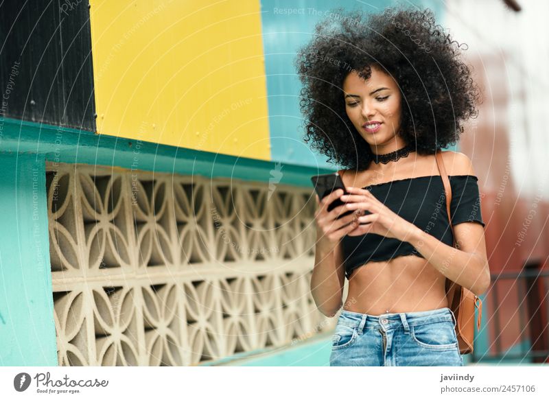 Frau mit Afro-Haaren auf der Straße, die ein Smartphone hält. Lifestyle Stil Freude Glück schön Haare & Frisuren Telefon PDA Technik & Technologie Mensch