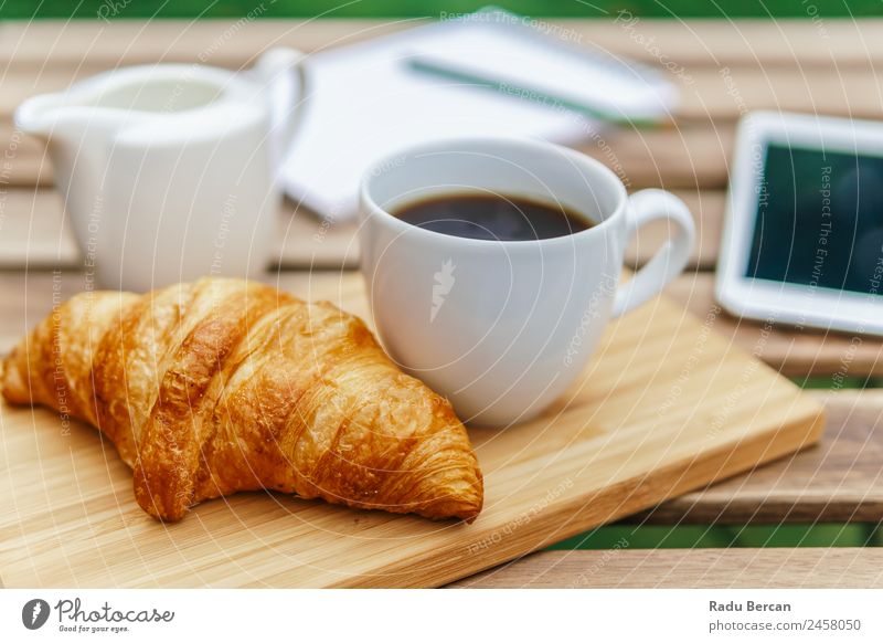 Frühstück am Morgen im Grünen Garten mit französischem Croissant, Kaffeetasse, Orangensaft, Tablette und Notizbuch auf Holztisch Tisch Hintergrundbild Sommer