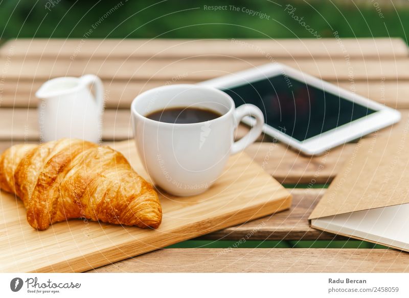 Frühstück am Morgen im Grünen Garten mit französischem Croissant, Kaffeetasse, Orangensaft, Tablette und Notizbuch auf Holztisch Tisch Hintergrundbild Sommer