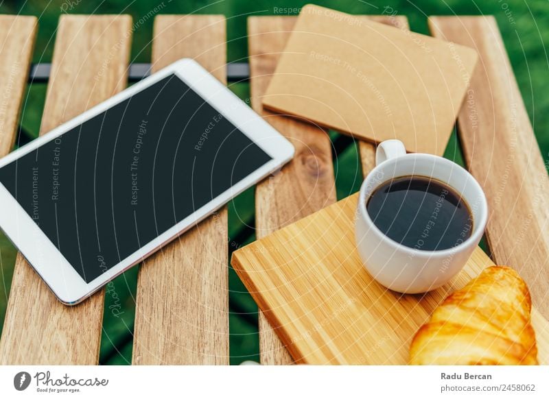 Frühstück am Morgen im Grünen Garten mit französischem Croissant, Kaffeetasse, Orangensaft, Tablette und Notizbuch auf Holztisch Tisch Hintergrundbild Sommer