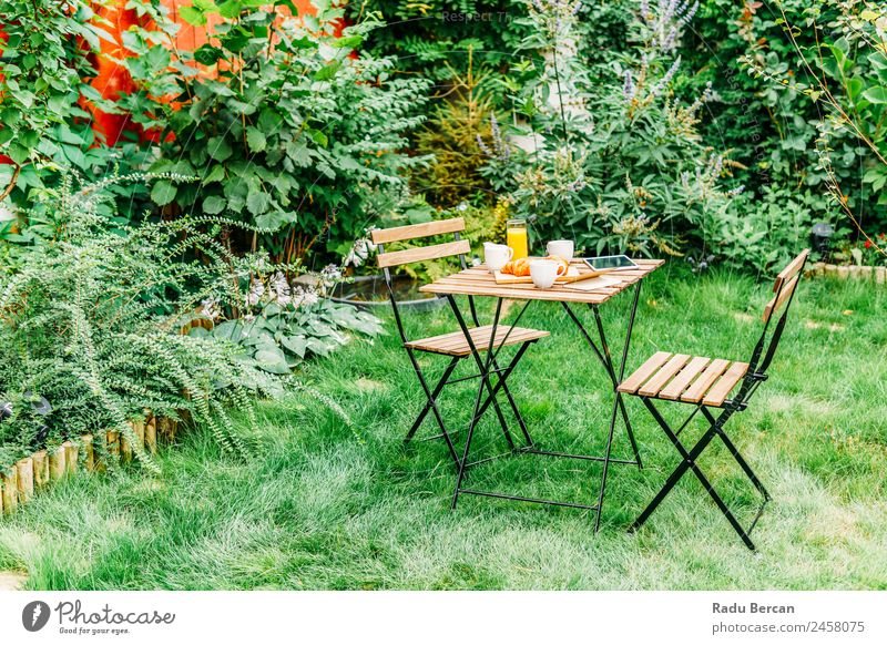 Frühstück am Morgen im Grünen Garten mit französischem Croissant, Kaffeetasse, Orangensaft, Tablette und Notizbuch auf Holztisch Tisch Hintergrundbild Sommer