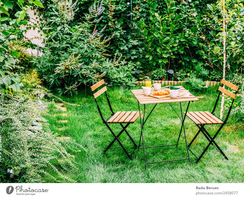 Frühstück am Morgen im Grünen Garten mit französischem Croissant, Kaffeetasse, Orangensaft, Tablette und Notizbuch auf Holztisch Tisch Hintergrundbild Sommer