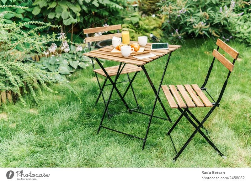 Frühstück am Morgen im Grünen Garten mit französischem Croissant, Kaffeetasse, Orangensaft, Tablette und Notizbuch auf Holztisch Tisch Hintergrundbild Sommer