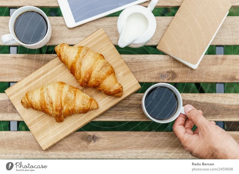 Frühstück am Morgen im Grünen Garten mit französischem Croissant, Kaffeetasse, Orangensaft, Tablette und Notizbuch auf Holztisch Tisch Hintergrundbild weiß