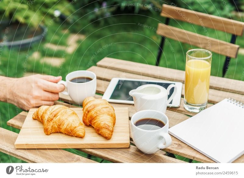 Frühstück am Morgen im Grünen Garten mit französischem Croissant, Kaffeetasse, Orangensaft, Tablette und Notizbuch auf Holztisch Tisch Hintergrundbild weiß