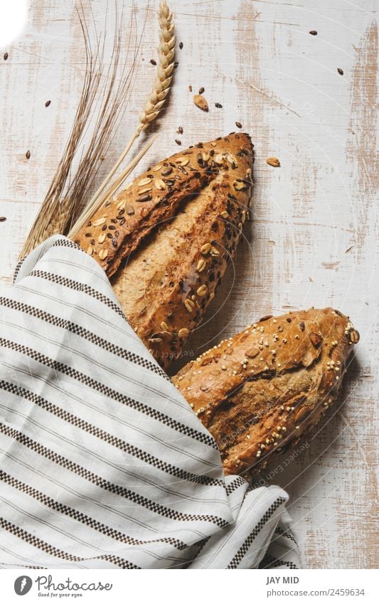 rustikales Saatgutbrot, umhüllt von gestreiftem Stoff Lebensmittel Brot Frühstück Bioprodukte Diät Menschengruppe frisch braun weiß Tradition Brote Brotlaib