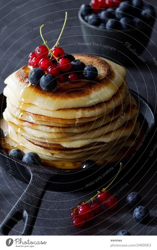 Süße Pfannkuchen mit Johannisbeeren, Blaubeeren und leckerem Ahornsirup in gusseiserner schwarzer Pfanne Lebensmittel Zuckersirup Frucht Teigwaren Backwaren