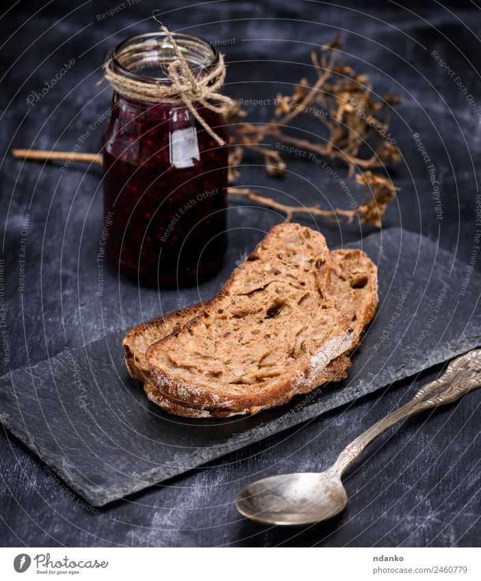 Roggenbrot und ein Glas Himbeermarmelade Brot Süßwaren Marmelade Frühstück Löffel Essen schwarz Spielfigur Lebensmittel Hintergrund süß Farbfoto Menschenleer