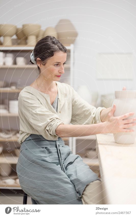 Junge Frau sitzt am Tisch und stellt Ton- oder Keramikbecher her. Geschirr Freizeit & Hobby Handarbeit Arbeit & Erwerbstätigkeit Beruf Handwerker Arbeitsplatz