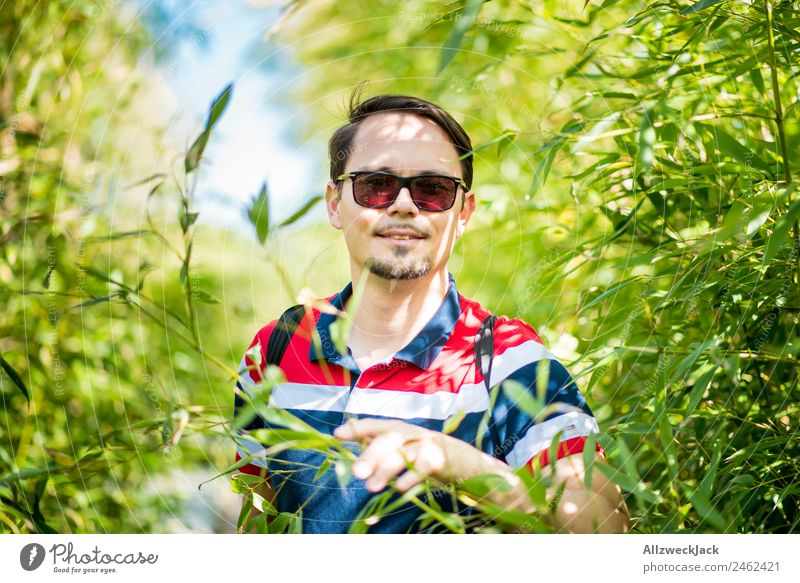 Portrait von einem jungen Mann im Bambus Dschungel Porträt Junger Mann 1 Mensch Sonnenbrille grün Natur Tag Sträucher Blatt Wald Urwald Ferien & Urlaub & Reisen