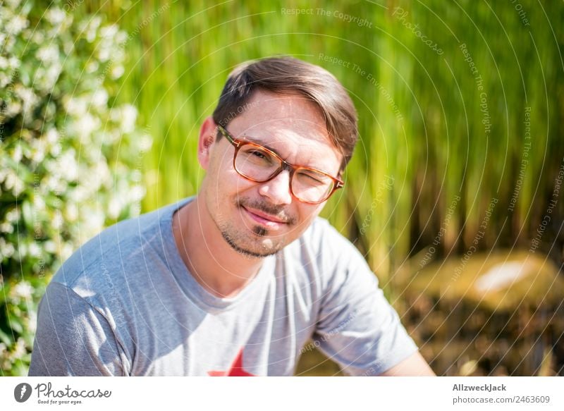 junger Mann mit Brille lächelt in Kamera 1 Mensch Junger Mann Porträt Brillenträger Lächeln sympathisch Fröhlichkeit Freundlichkeit Natur grün Schönes Wetter