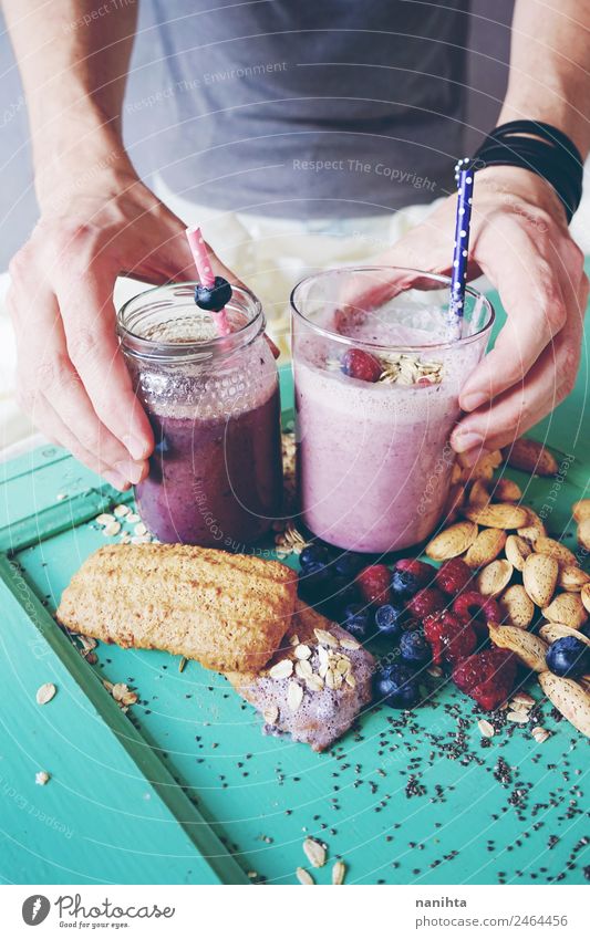 Mann, der zwei Beeren-Smoothies hält. Lebensmittel Frucht Getreide Teigwaren Backwaren Mandel Chia Plätzchen Hafer Milchshake Ernährung Essen Frühstück