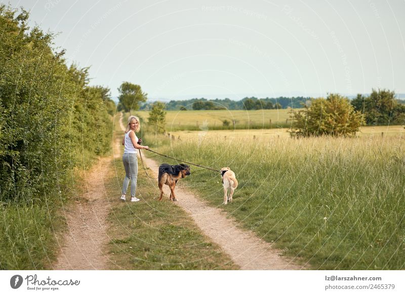 Junge blonde Frau geht mit ihren beiden Hunden spazieren. Lifestyle Glück schön Sommer Erwachsene Freundschaft 1 Mensch Natur Tier Wärme Gras Park Haustier