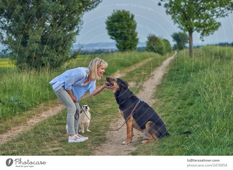 Lächelnde Frau, die ihren Hund auf der Landstraße streichelt. Sommer Erwachsene Freundschaft Landschaft Tier Wege & Pfade blond lachen Lehre ländlich