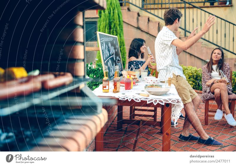 Junge Leute, die im Freien reden und im Ofen kochen. Wurstwaren Mittagessen Alkohol Bier Lifestyle Freude Glück Erholung Freizeit & Hobby Sommer Garten Tisch