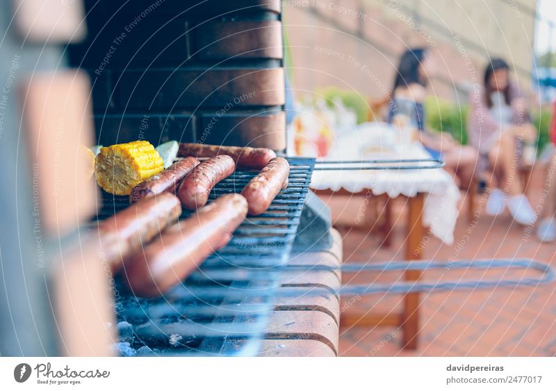 Würstchen und Maiskolben im Grill gekocht Wurstwaren Gemüse Mittagessen Lifestyle Freude Glück Erholung Freizeit & Hobby Sommer Garten Tisch sprechen Frau