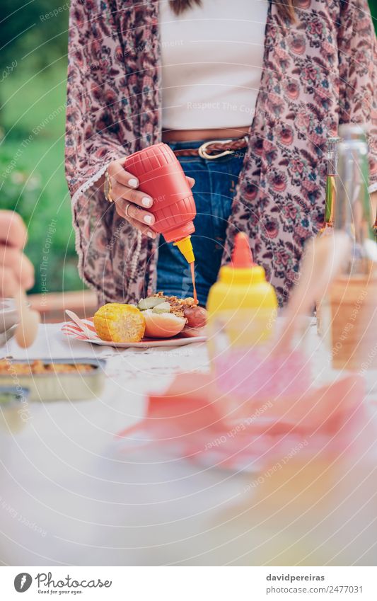 Frau Hand gießt Ketchup über einen amerikanischen Hot Dog. Fleisch Wurstwaren Brot Brötchen Mittagessen Fastfood Bier Teller Flasche Lifestyle Freude Glück