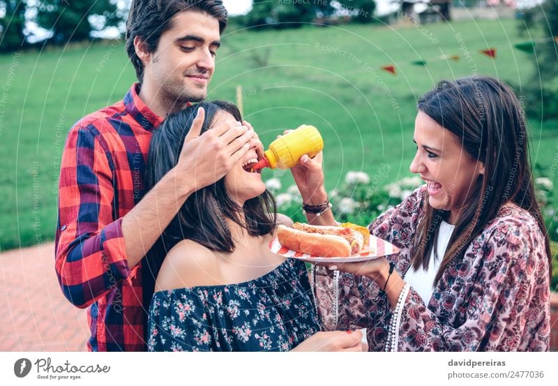 Mann hält Hot Dog im Barbecue mit Freunden. Wurstwaren Essen Fastfood Teller Lifestyle Freude Glück Sommer Frau Erwachsene Freundschaft Mund Hand genießen