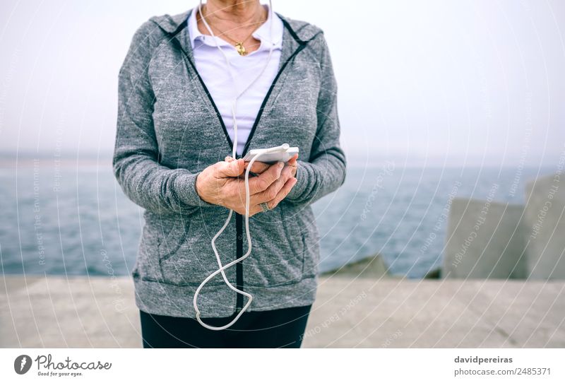 Senior-Sportlerin hält ihr Smartphone in der Hand. Lifestyle Freizeit & Hobby Meer Dekoration & Verzierung Musik Telefon PDA Technik & Technologie Mensch Frau