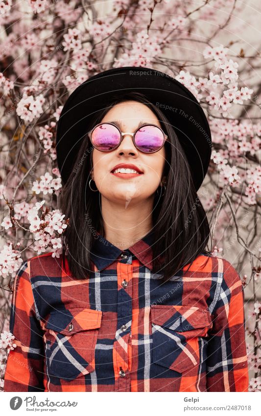 Brünettes Mädchen bei einem Mandelbaum Stil Glück schön Gesicht Garten Mensch Frau Erwachsene Natur Baum Blume Blüte Park Mode Sonnenbrille Hut brünett Lächeln