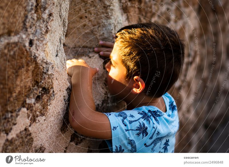 Kleiner Junge schaut durch die Mauer einer Burg. Gesicht Spielen Kind Mensch Mann Erwachsene Kindheit Gras Felsen Gipfel Dorf Kirche Burg oder Schloss Ruine