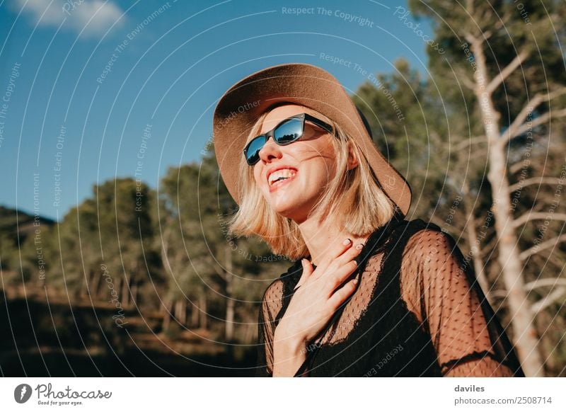 Glückliche blonde Frau mit Sonnenbrille und Hut, die die Sonne in der Natur genießt Lifestyle elegant Stil Freude schön Erholung Ferien & Urlaub & Reisen