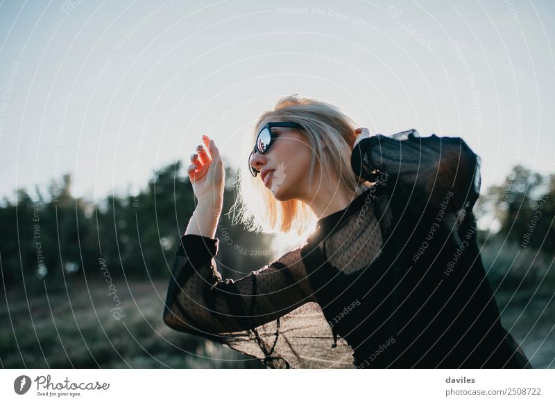 Blonde Frau mit schwarzem Kleid und Sonnenbrille führt im Gegenlicht Tanz in der Natur auf Lifestyle elegant Stil Freude schön Wellness Leben stimmig Wohlgefühl