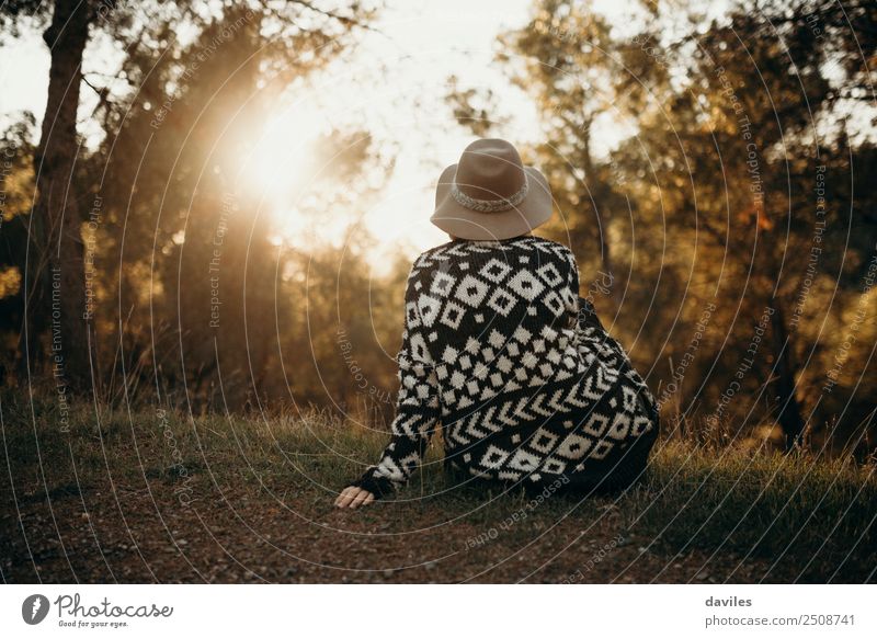 Frau mit Hut auf dem Rücken, die bei Sonnenuntergang im Wald in die Sonne schaut Lifestyle Wellness Wohlgefühl Erholung Ferien & Urlaub & Reisen Abenteuer