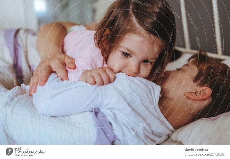 Kleines Mädchen spielt über dem Jungen, der im Bett liegt. Lifestyle Freude Glück Erholung Freizeit & Hobby Spielen Schlafzimmer Kind Baby Frau Erwachsene