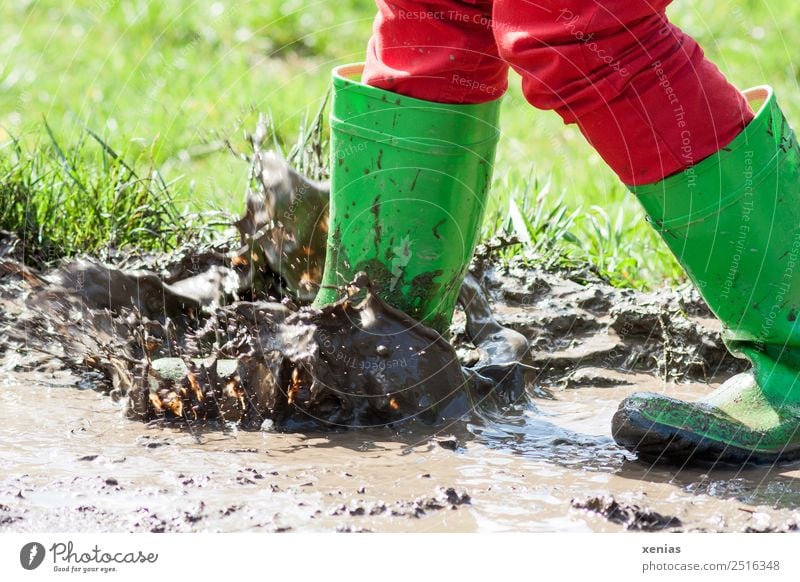 Mit grünen Gummistiefel in der Pfütze matschen Freude Kind Kindheit Beine 1 Mensch 3-8 Jahre 8-13 Jahre Jeanshose Stiefel springen dreckig braun rot stampfen