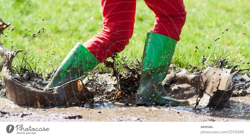 Durch Schlamm laufen mit grünen Gummistiefeln, so dass es spritzt Beine Gras spritzen Hose Matsch Jeanshose Stiefel gehen Spielen springen toben dreckig braun